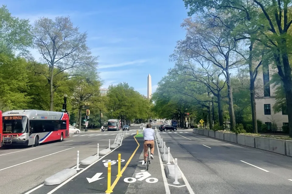 Cyclist on protected bike lane in middle of street in Washington D.C. with Washington Monument obelisk visible in background.